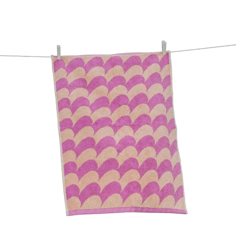 Towel with pink and beige wave pattern hanging on a line against a blue sky.