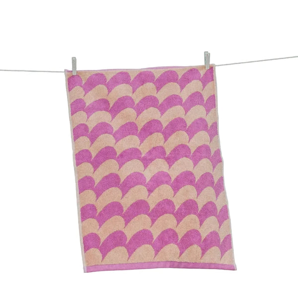 Towel with pink and beige wave pattern hanging on a line against a blue sky.