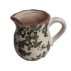 Ceramic pitcher with green floral pattern on a white background